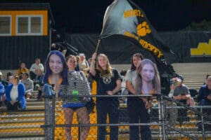 Fans cheering at a field hockey game, holding cutouts and a North Field Hockey flag in the stands.