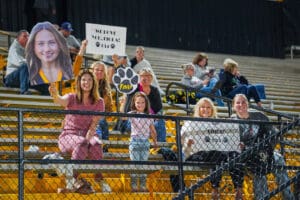 Enthusiastic fans in the stands cheering with signs at a sports event.