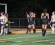 Field hockey players celebrating a goal under stadium lights.