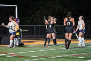 Field hockey players celebrating a goal under stadium lights.