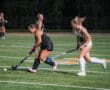 Two field hockey players competing for the ball during a nighttime match on a grassy field.
