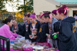 Group of girls with pink ribbons buying treats at an outdoor bake sale.