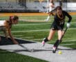 Two field hockey players compete for the ball during a match on a grassy field.