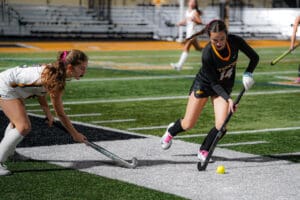 Two field hockey players compete for the ball during a match on a grassy field.