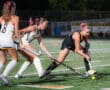 Field hockey players compete for ball under night stadium lights.