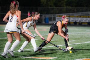 Field hockey players compete for ball under night stadium lights.