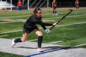 Field hockey player prepares to strike the ball on a green sports field during a game.