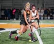 Two field hockey players in action on a turf field during a competitive match.