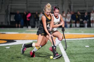 Two field hockey players in action on a turf field during a competitive match.