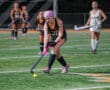 Female field hockey player focuses on ball control during a night match on the turf.