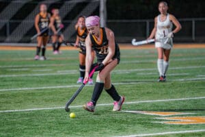 Female field hockey player focuses on ball control during a night match on the turf.