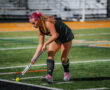 Female field hockey player prepares to strike ball during a game at night.