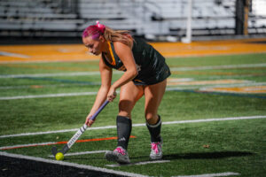 Female field hockey player prepares to strike ball during a game at night.