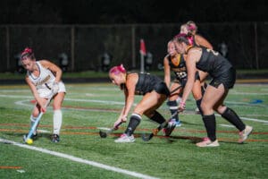 Field hockey game at night with players competing for the ball on a turf field.