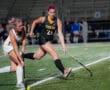 Two female field hockey players in action during a night match on the field.