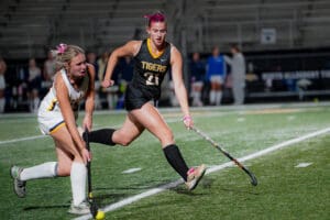Two female field hockey players in action during a night match on the field.