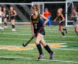 Field hockey player in black Tigers jersey dribbles during a match on green turf field.