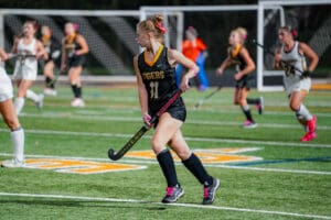 Field hockey player in black Tigers jersey dribbles during a match on green turf field.