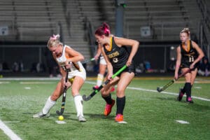 Girls playing field hockey under stadium lights, focused on the ball.