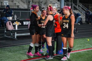 High school girls' field hockey team celebrating on the field in matching uniforms and pink bows.