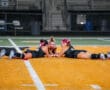 Three female athletes lie on a sports field, engaged in a focused discussion or game strategy session.