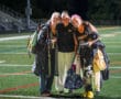 Three field hockey players in Tigers jerseys smiling and posing on a sports field at night.