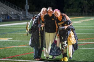 Three field hockey players in Tigers jerseys smiling and posing on a sports field at night.
