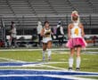 Two field hockey players in fun outfits warm up on a field, one wearing a pink tutu.