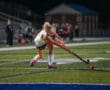 Field hockey player in action, striking the ball under stadium lights on the green turf.