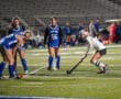 Field hockey players competing on turf at night under stadium lights.