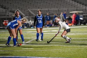 Field hockey players competing on turf at night under stadium lights.