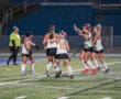 Field hockey team celebrating on the field under stadium lights.