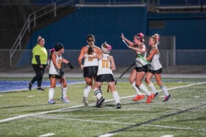 Field hockey team celebrating on the field under stadium lights.