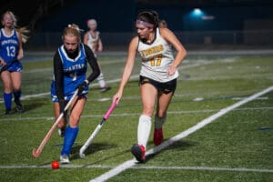 Two field hockey players from opposing teams in action on the field at night.