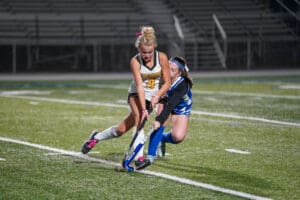 Two field hockey players compete for the ball on a grass field during a match.
