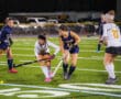 Field hockey match with players in action on a green turf field, focusing on intense competition.