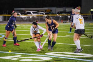 Field hockey match with players in action on a green turf field, focusing on intense competition.