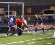 Girls' field hockey game with goalie and players in action on a green turf field.