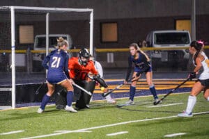 Girls' field hockey game with goalie and players in action on a green turf field.