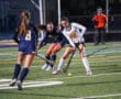 Girls playing competitive field hockey under stadium lights.