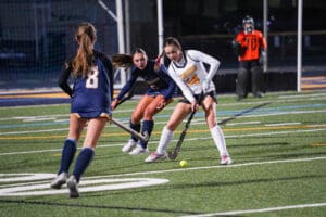 Girls playing competitive field hockey under stadium lights.