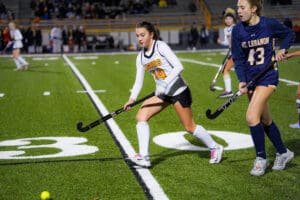 Girls playing field hockey on a sports field during a competitive match.