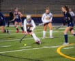 Field hockey players compete on a green field under stadium lights.