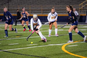 Field hockey players compete on a green field under stadium lights.