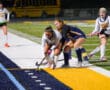 High school field hockey match at night, players competing for the ball on the sidelines.