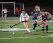 Field hockey players competing in a match on a green turf under stadium lights.