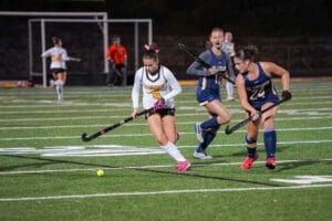 Field hockey players competing in a match on a green turf under stadium lights.