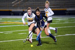 Girls playing field hockey on a turf field during a competitive match.