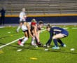 Field hockey players compete for the ball on the turf during a night game.