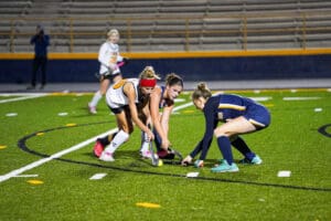 Field hockey players compete for the ball on the turf during a night game.